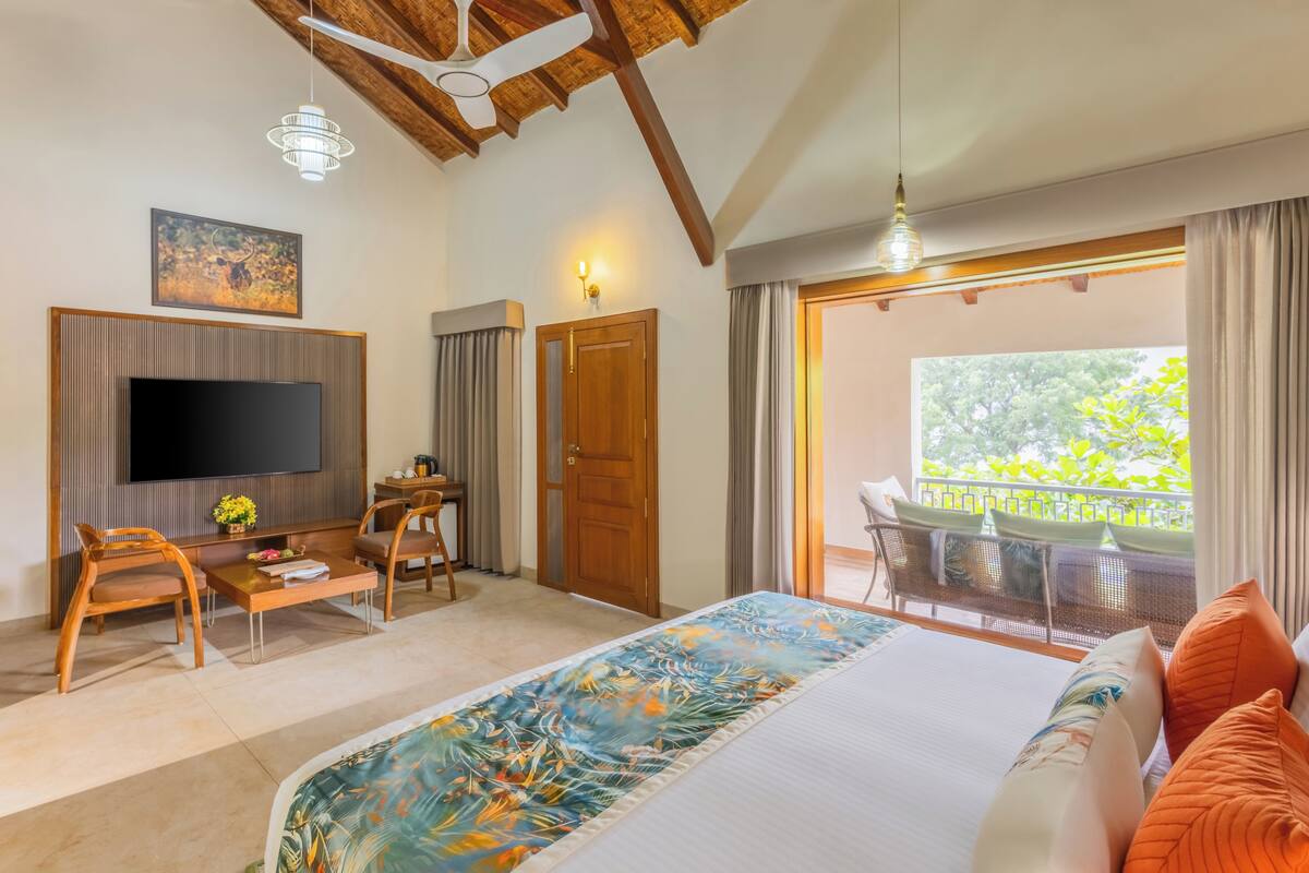 A bedroom with a large bed, a TV, a desk, and a balcony with a view.