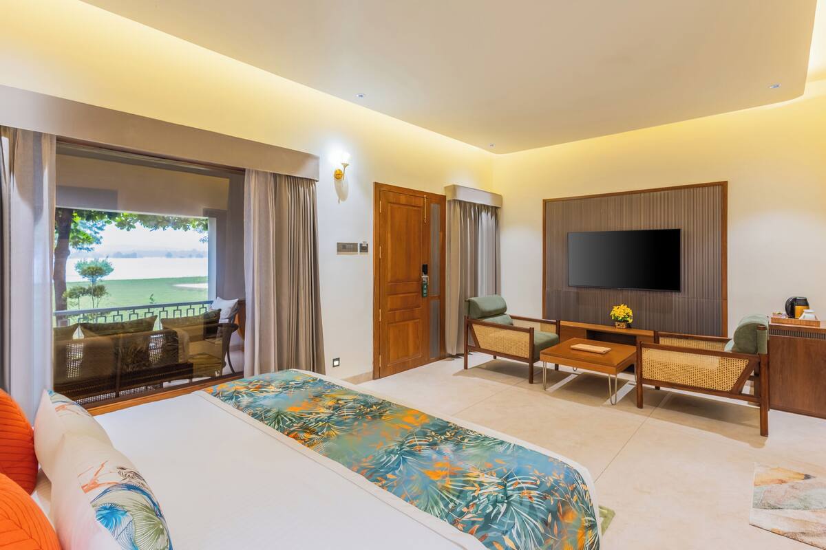 A hotel room with a bed, a TV, a seating area, and a balcony with a view.