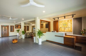 A hotel reception area with a wooden reception desk, potted plants, a seating area, and a wall with a framed artwork. - The Forest Chapter By Sayaji Madhai (Sarangpur)