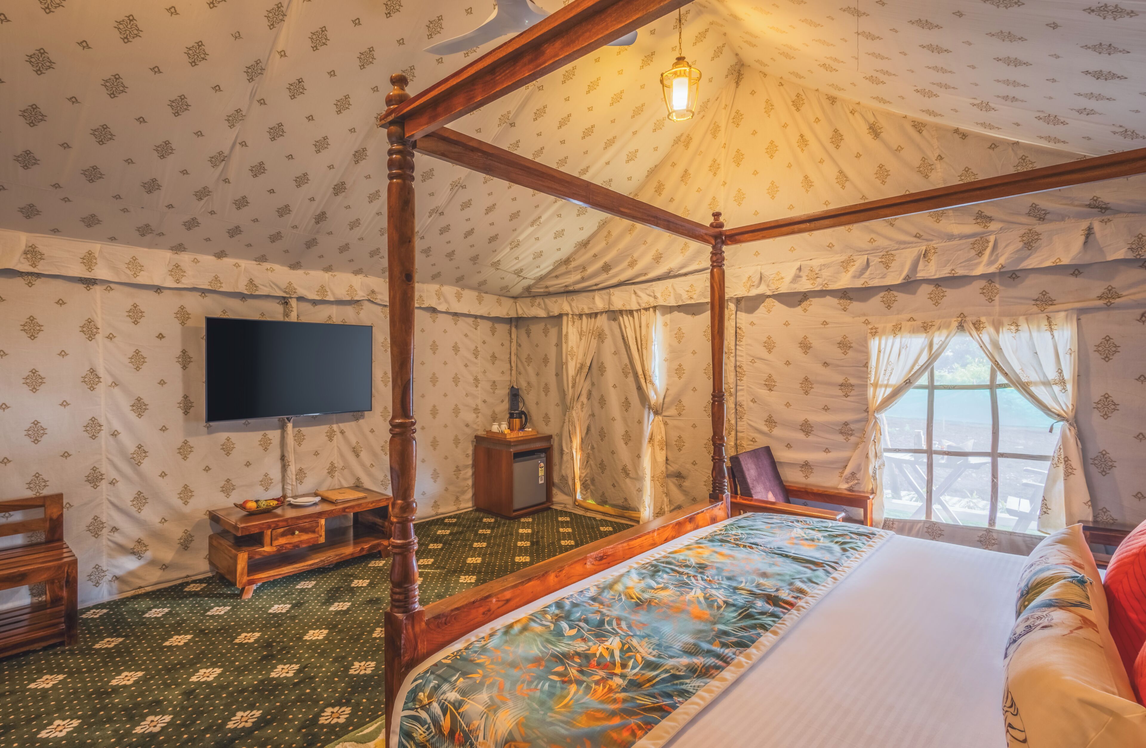 A four-poster bed with a television on the wall, a small wooden side table, and a window with curtains.