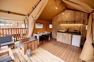 Una terraza de madera con comedor, una pequeña cocina americana y un sofá.