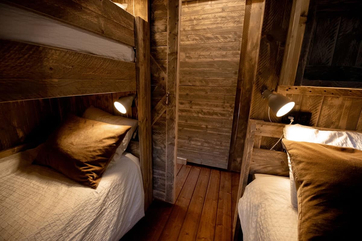 A rustic wooden room with two bunk beds, each with a bedside lamp.