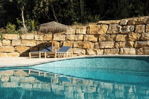 Una piscina cristalina con paredes de piedra y un paraguas de paja.