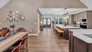 A modern kitchen with a large island, wooden flooring, and a dining area with a long table and chairs.