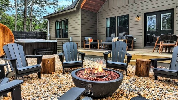 An outdoor patio with Adirondack chairs, a fire pit, and a deck area with seating.