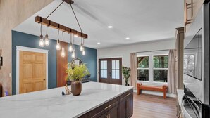 A modern kitchen with a large island, wooden cabinets, and pendant lighting.