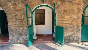 A stone building with two open green doors leading to a room with a tiled floor and a window. - Manoribel (Mumbai)