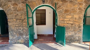 Un bâtiment en pierre doté de deux portes vertes ouvertes, qui donnent sur une pièce au sol carrelé et comportant une fenêtre.