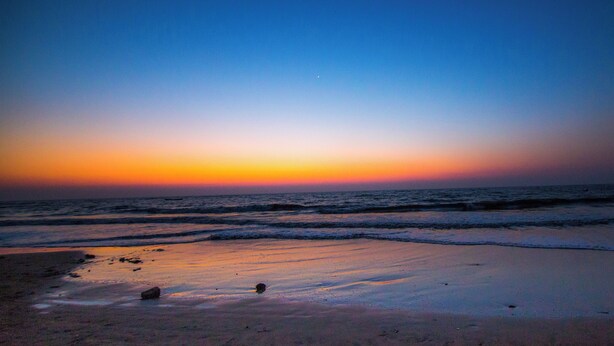 Een strand bij zonsondergang, met golven die zachtjes op het strand komen.'