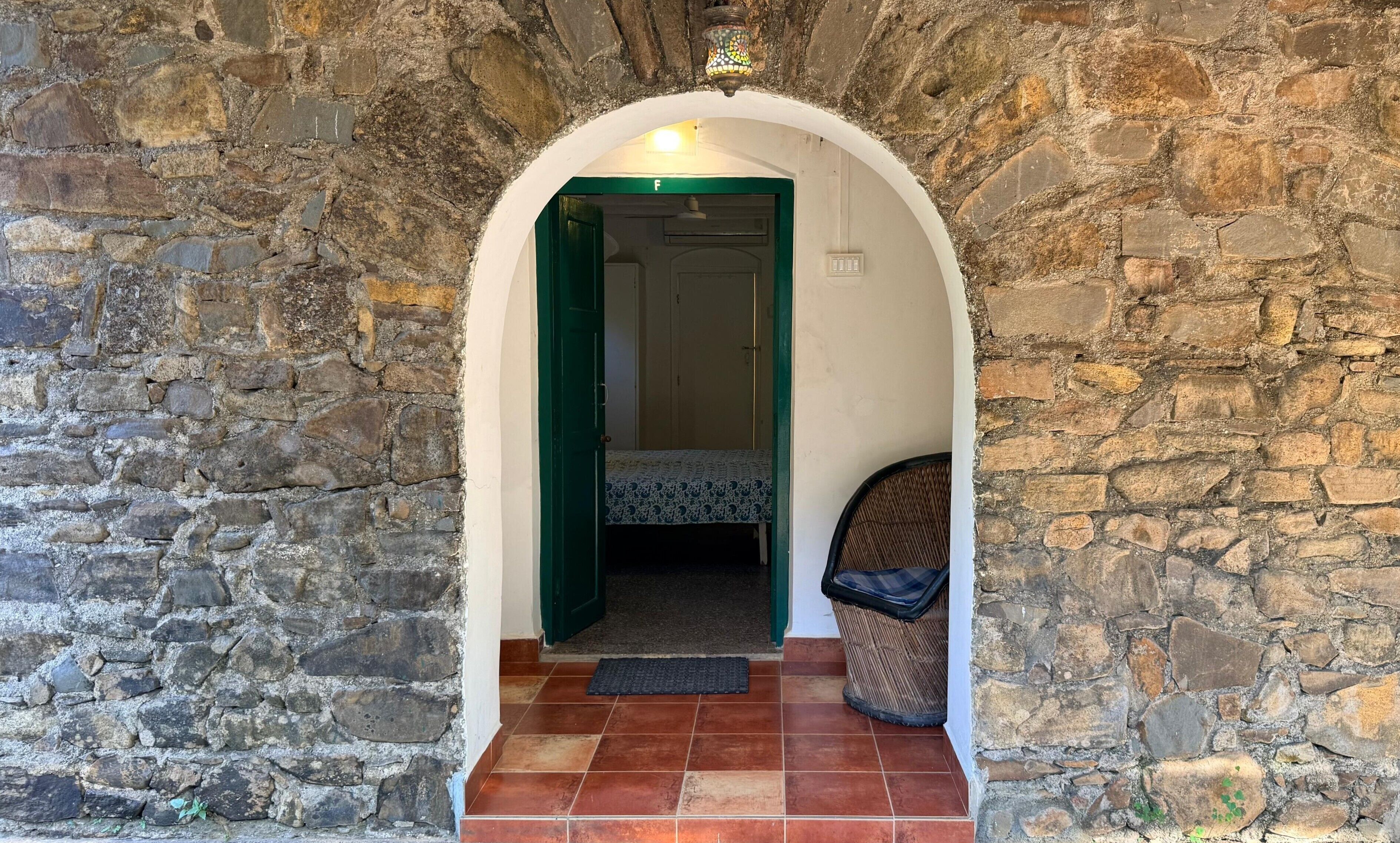 A stone archway leading to a room with a bed and a chair.