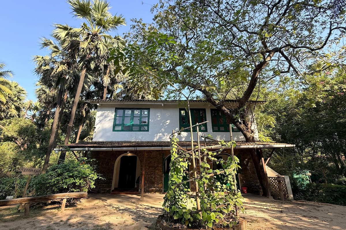 Une maison de campagne aux fondations en pierre, à l’extérieur blanc et aux encadrements de fenêtres verts.