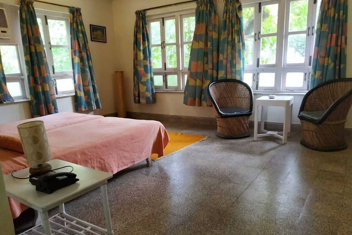 Una habitación con una cama, dos sillas, una mesita y una ventana con cortinas.
