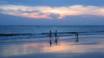 A beach scene with a sunset, waves, and silhouettes of people.
