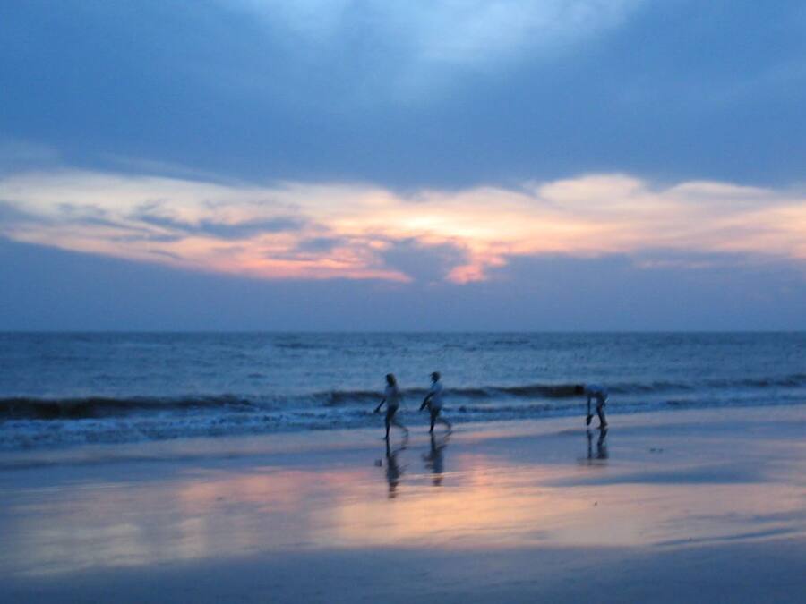 Escena de playa con atardecer, olas y siluetas de personas.