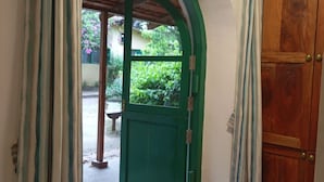 A doorway with a green arch and a wooden door, leading to an outdoor area with a bench and greenery. - Manoribel (Mumbai)