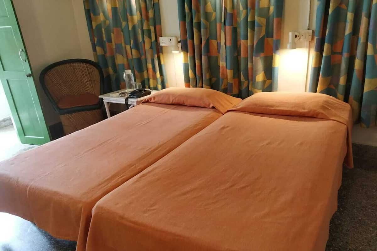 Un lit double avec une literie orange, une chaise, une petite table avec une lampe et des rideaux à motifs.