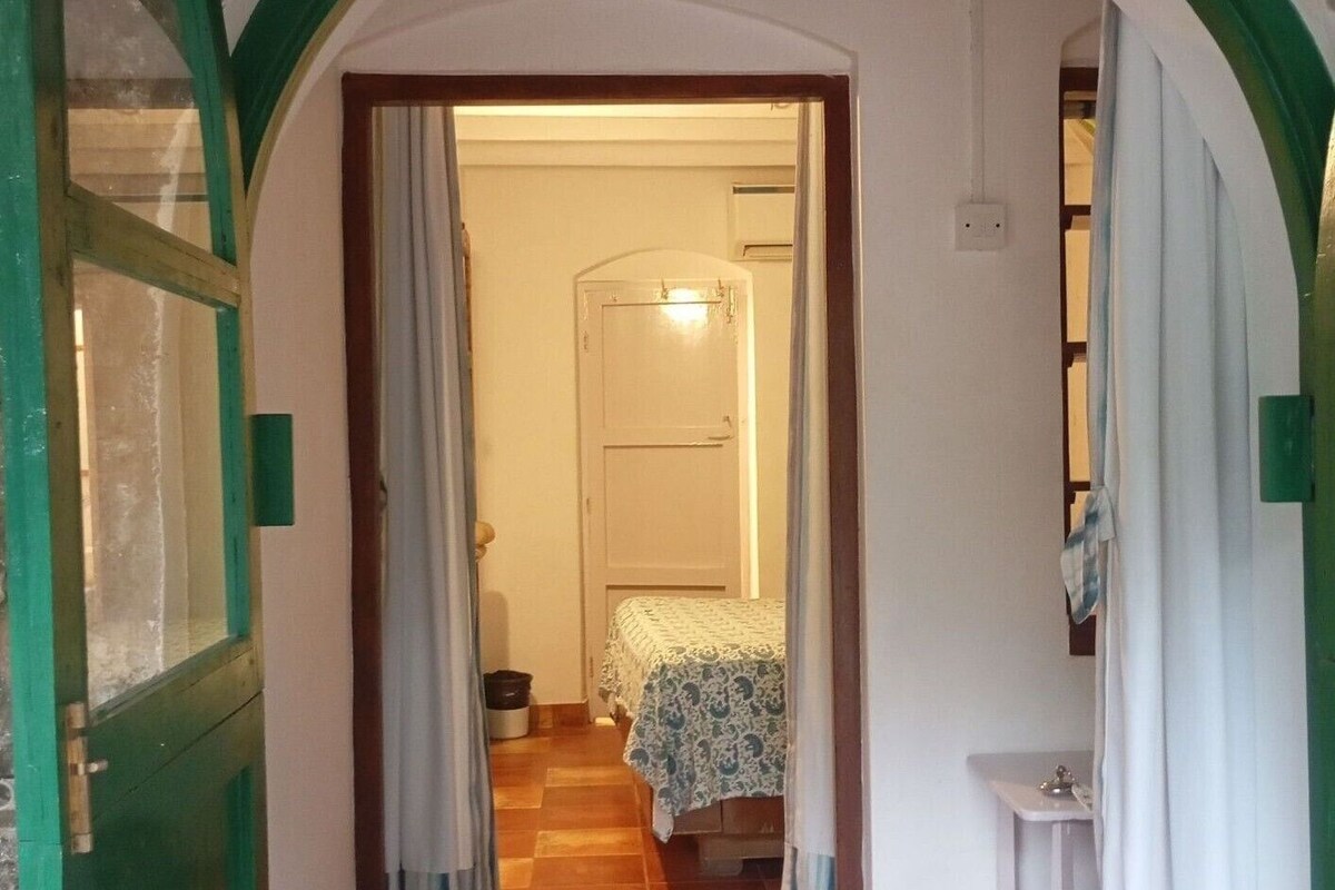 Un estrecho pasillo con suelo de baldosas que conduce a un dormitorio con cama y mesita de noche.
