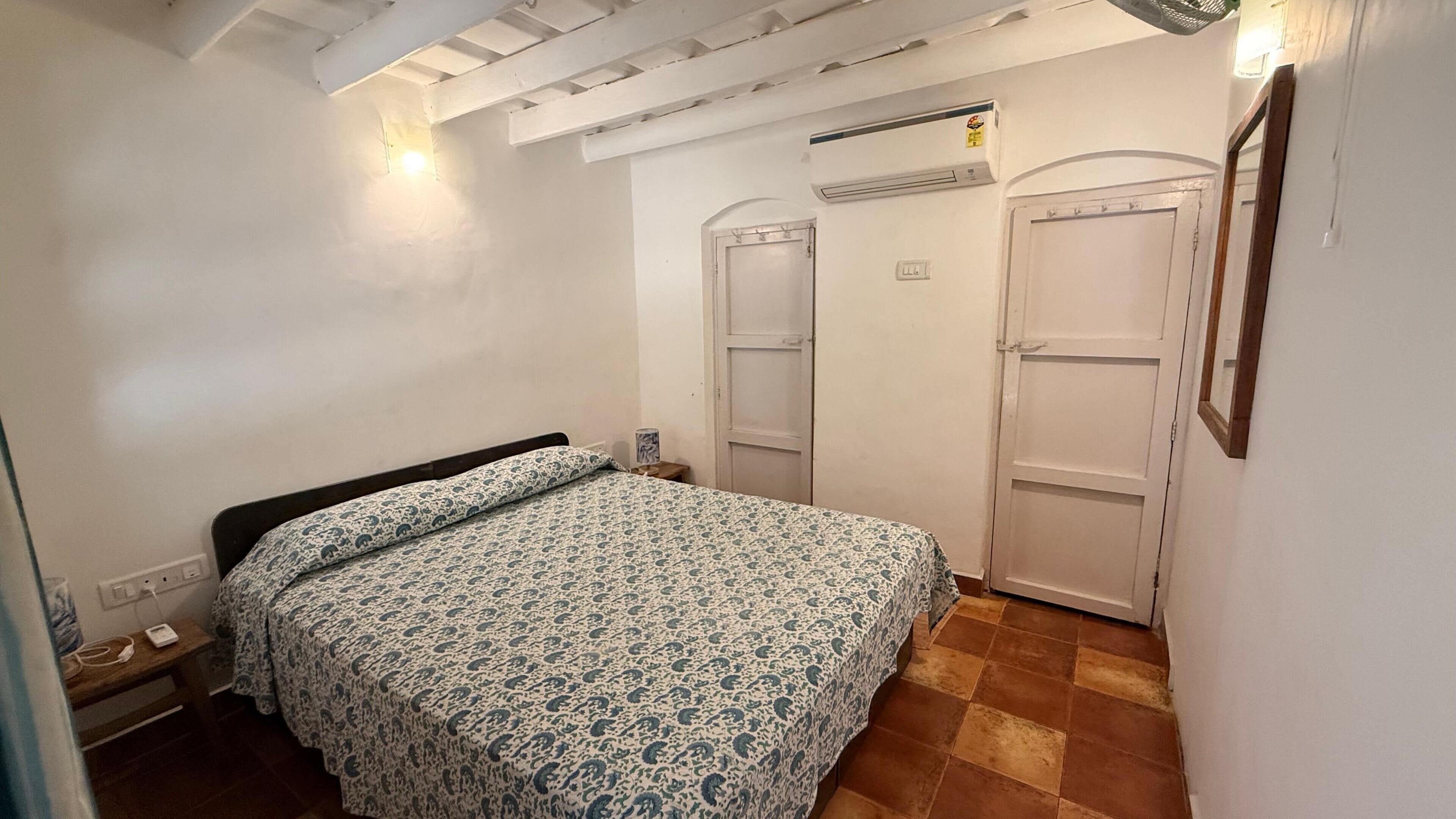 Un dormitorio con cama, dos puertas, un equipo de aire acondicionado e iluminación empotrada en la pared.