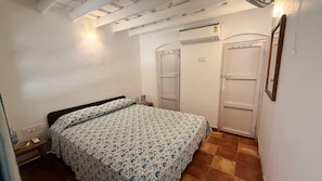 Une chambre à coucher comprenant un lit, deux portes, un appareil de climatisation et un luminaire fixé au mur.