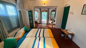 A hotel room with a bed, a small table with a chair, a window with curtains, and a view of the outside. - Manoribel (Mumbai)