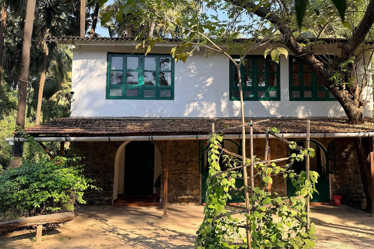 Une maison à deux étages, avec un toit en tuiles, des encadrements de fenêtres verts et des fondations en pierre.