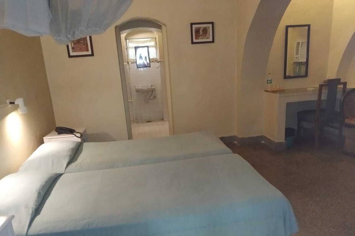 Une chambre avec deux lits, un bureau, une chaise, un miroir et une porte donnant sur une salle de bain.