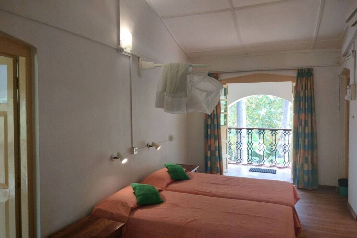 Une chambre avec deux lits, un balcon doté d’une rambarde et une fenêtre avec des rideaux.