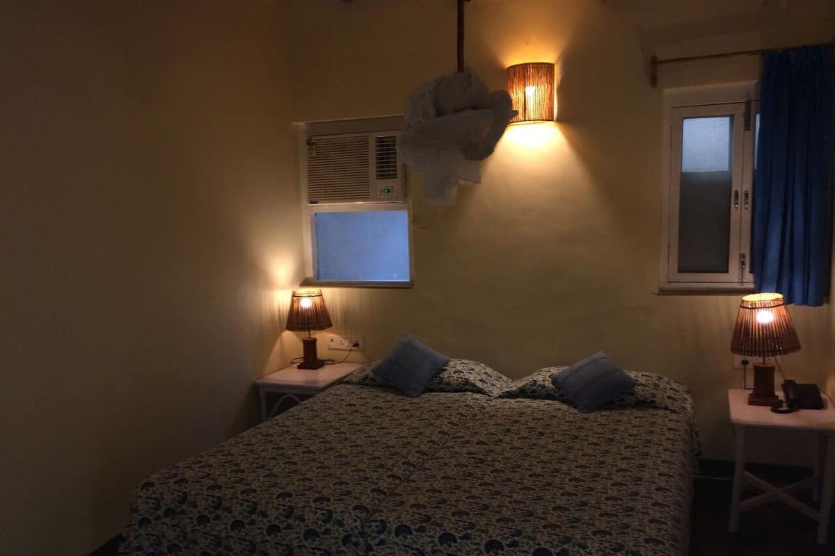 Une chambre à coucher avec un lit, deux tables de chevet avec des lampes, une fenêtre avec des rideaux et un climatiseur fixé au mur.