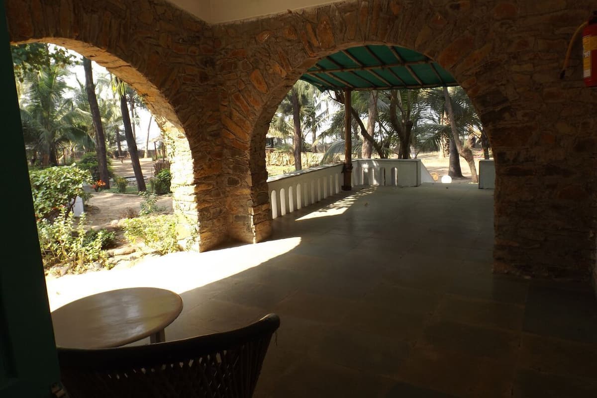 Un espace extérieur abrité, doté d’arches en pierre, d’un sol carrelé et offrant une vue sur des palmiers et une végétation luxuriante.