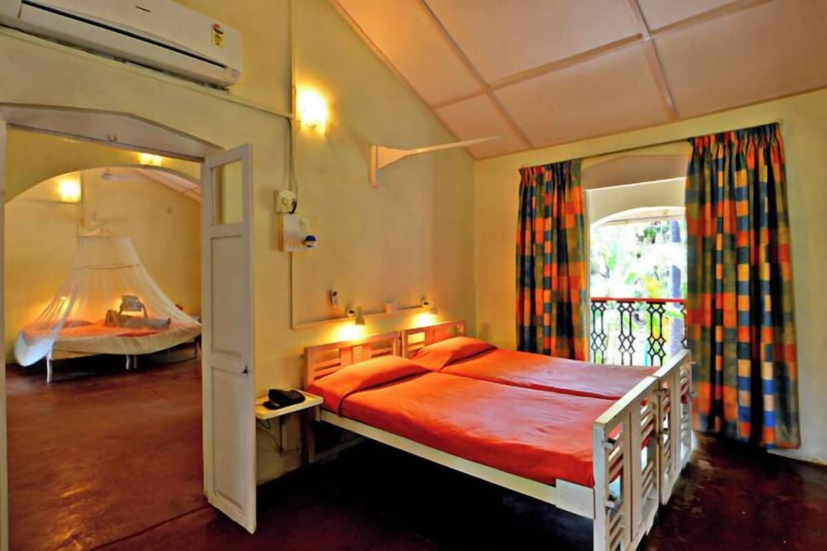 Une chambre avec deux lits, une moustiquaire, un climatiseur et un balcon agrémenté de rideaux colorés.