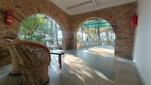 A covered outdoor area with stone walls, a wicker chair, and a table. - Manoribel (Mumbai)