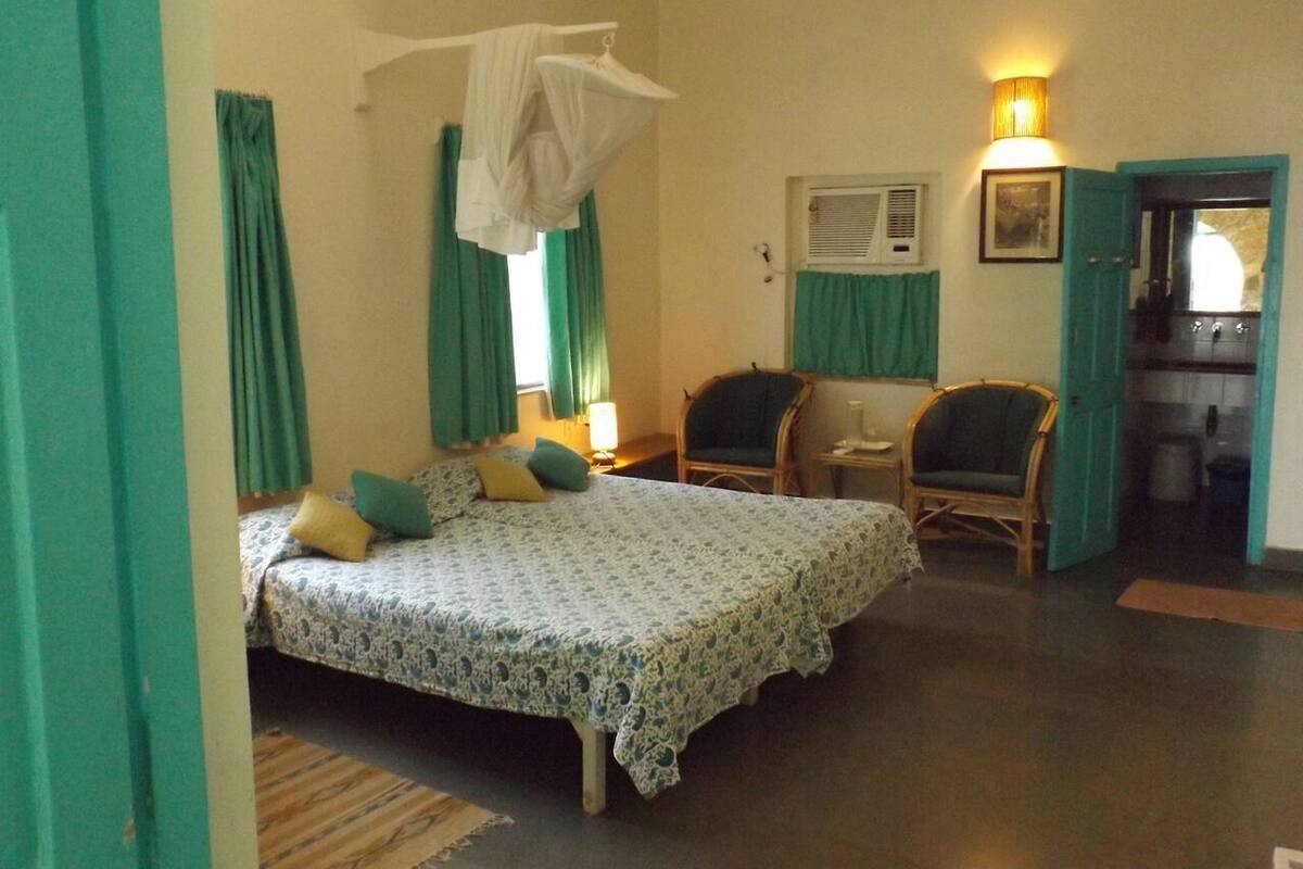 Une chambre à coucher avec un lit, deux chaises, une table de chevet et une fenêtre avec des rideaux.