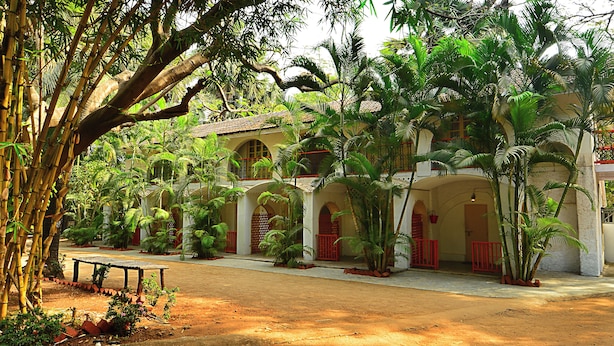 A colonial-style building with arched windows and a courtyard surrounded by lush greenery and palm trees. - Manoribel (Mumbai)