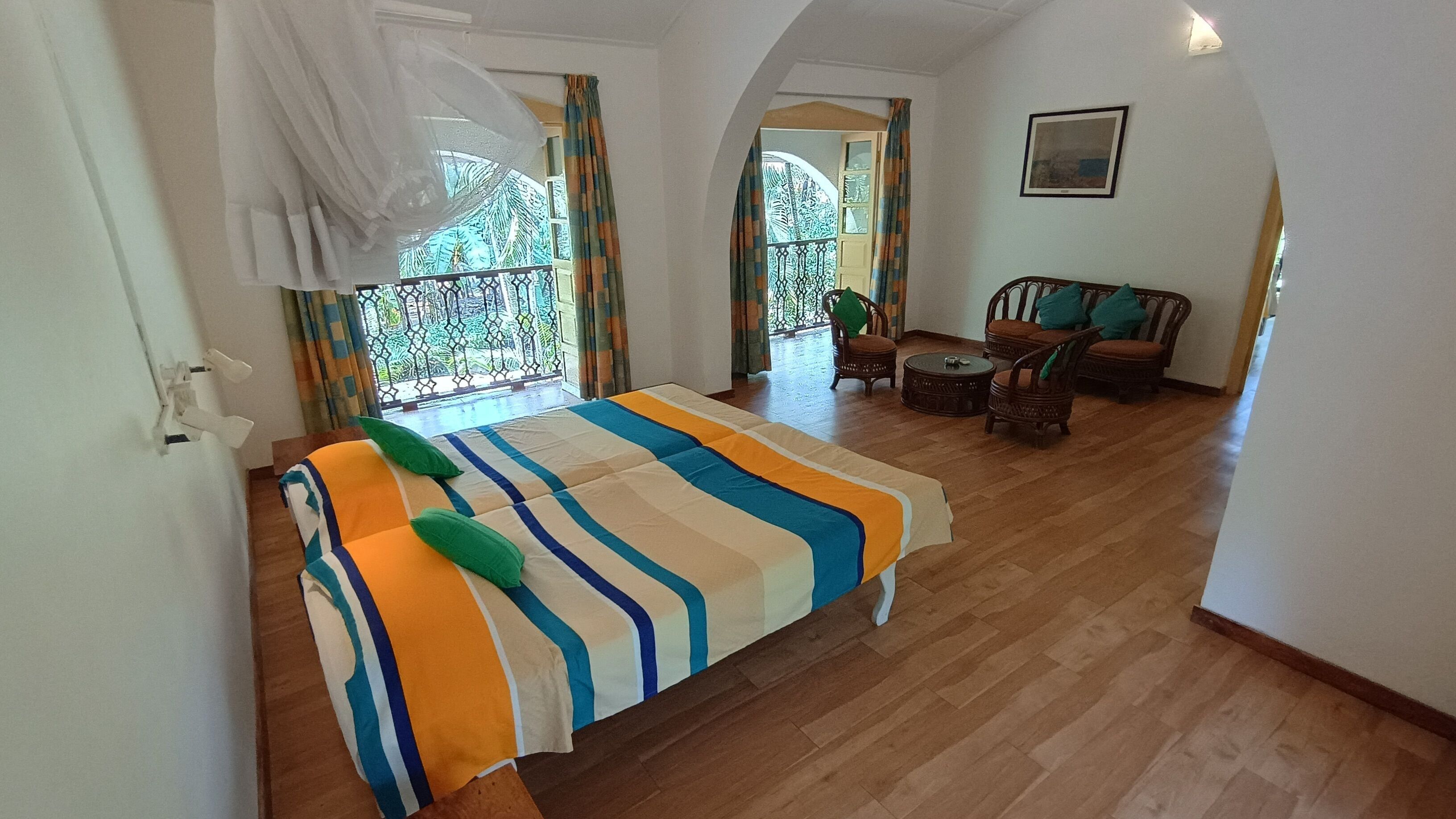 Une chambre à coucher avec un lit, un balcon et un coin salon avec des fauteuils.