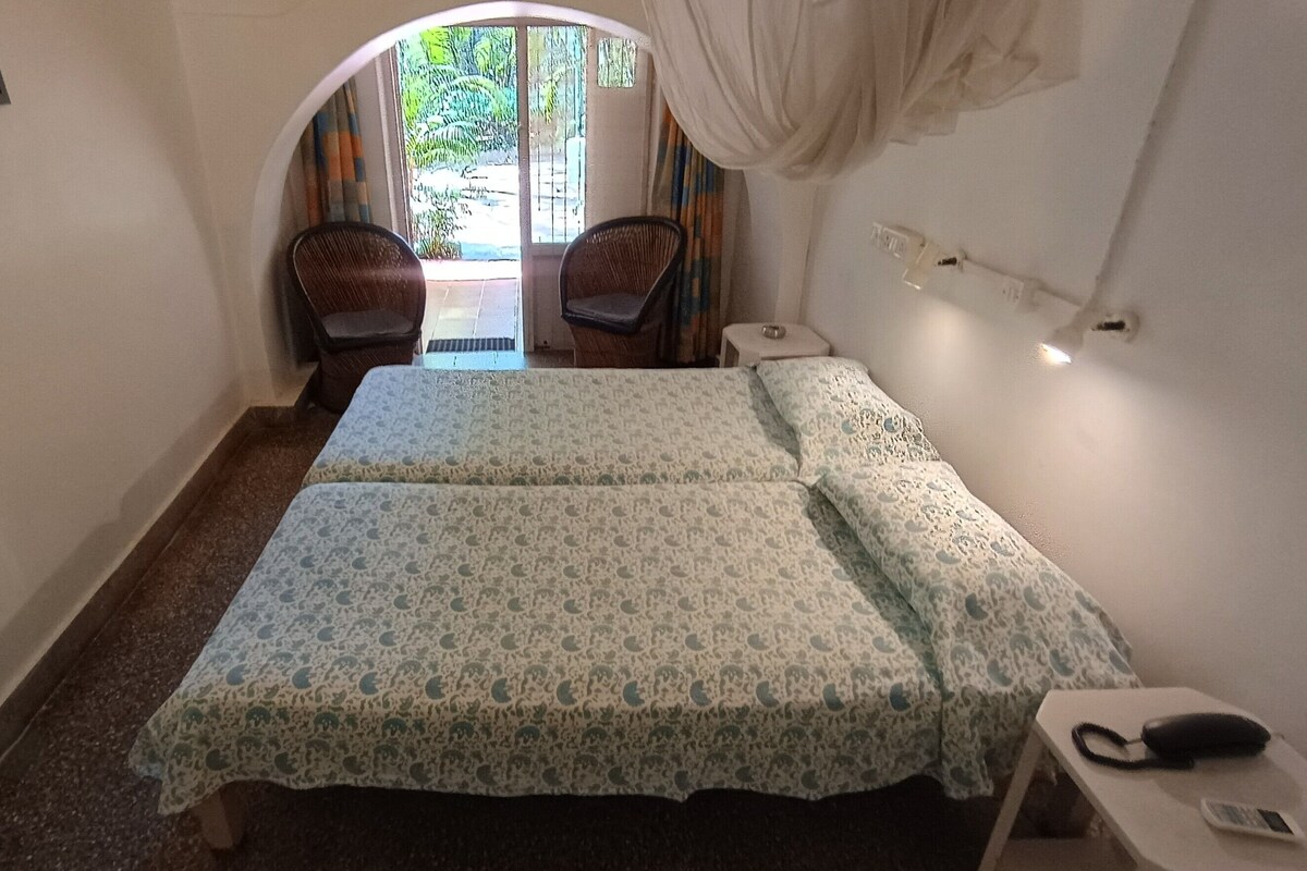 A room with two beds, a small table with a phone, and a view of the outdoors through a doorway.