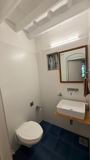Une salle de bain avec des toilettes blanches, un lavabo surmonté d’un miroir et un sol carrelé de carreaux bleus.