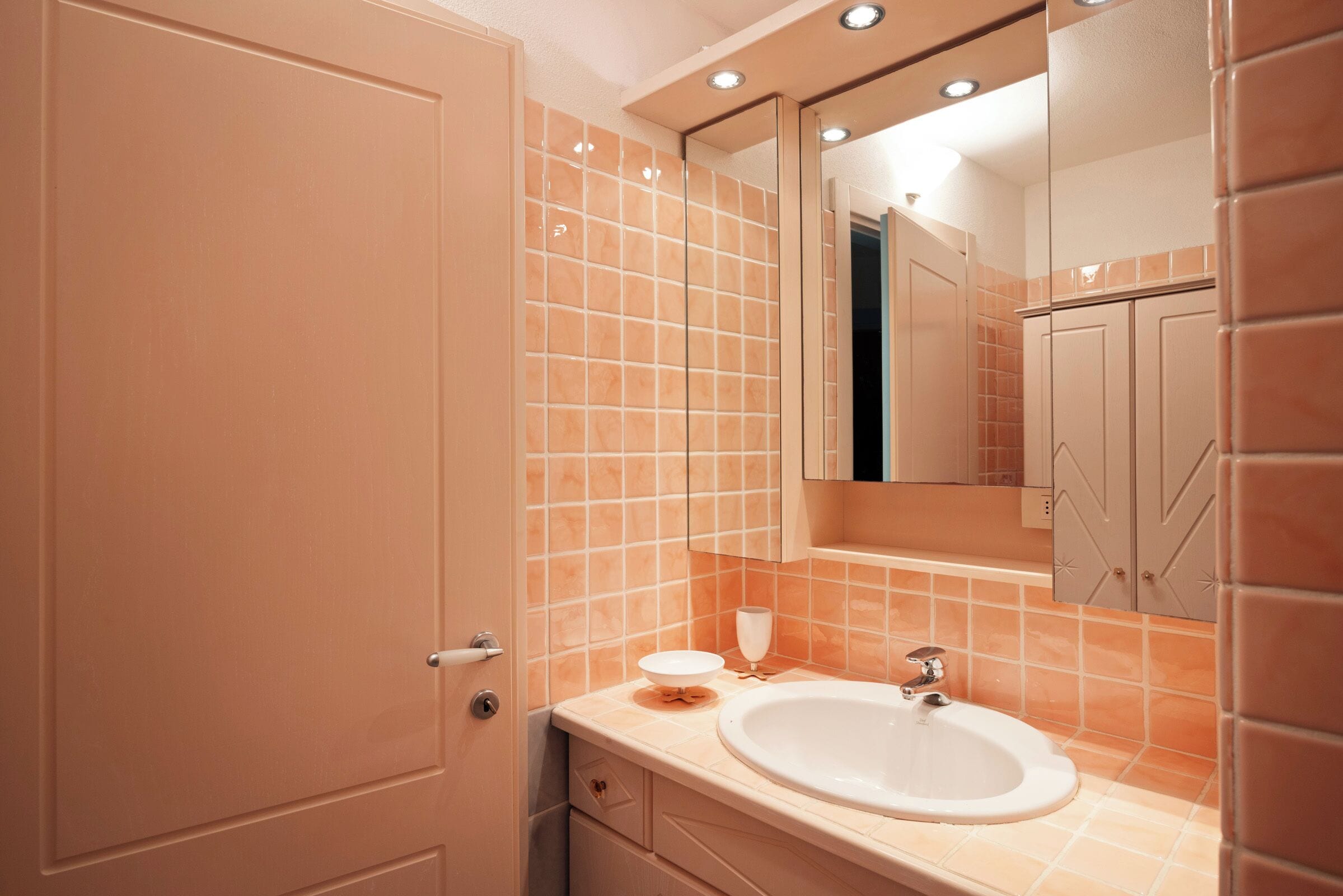A bathroom with a white sink, a mirror above it, and orange-tiled walls.