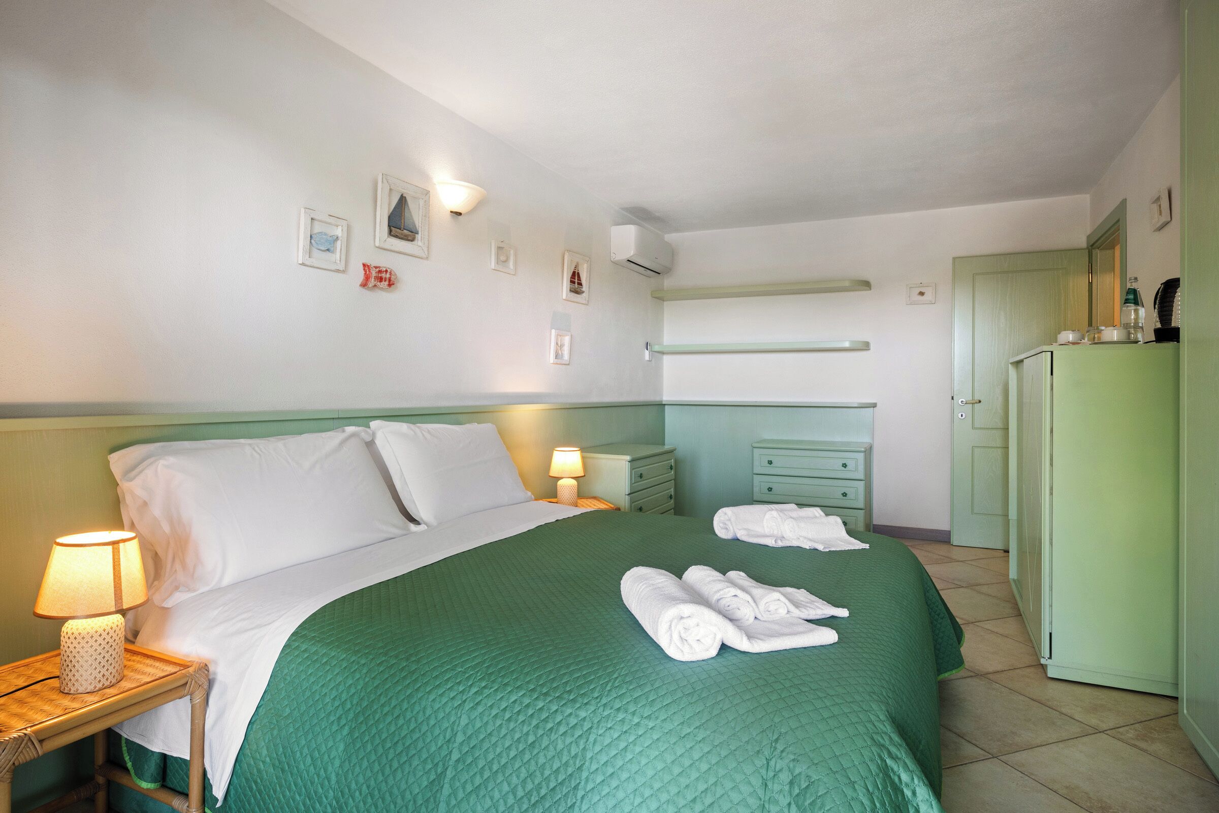 A hotel room with a bed, a nightstand with a lamp, a dresser, and a wardrobe.