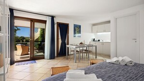 Habitación de hotel con cama, mesa de comedor, zona de cocina y puerta corrediza de vidrio que da a un espacio exterior.