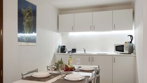 Cocina compacta con alacenas blancas, microondas y comedor dispuesto con platos, vasos y un frutero.