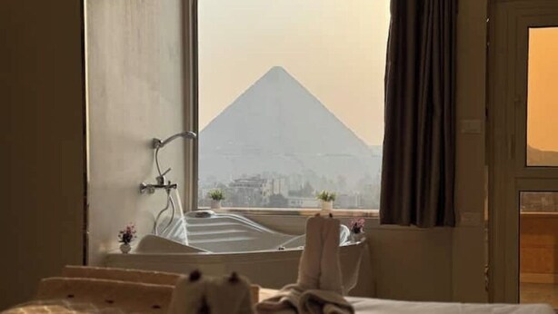 A hotel room with a bed, a window, and a view of a pyramid. - King Khufu suite (Giza Governorate)