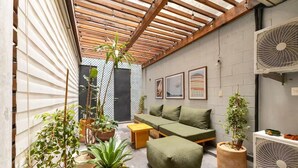Un espacio interior acogedor con techo de madera, un sofá verde, una mesita y varias macetas con plantas.