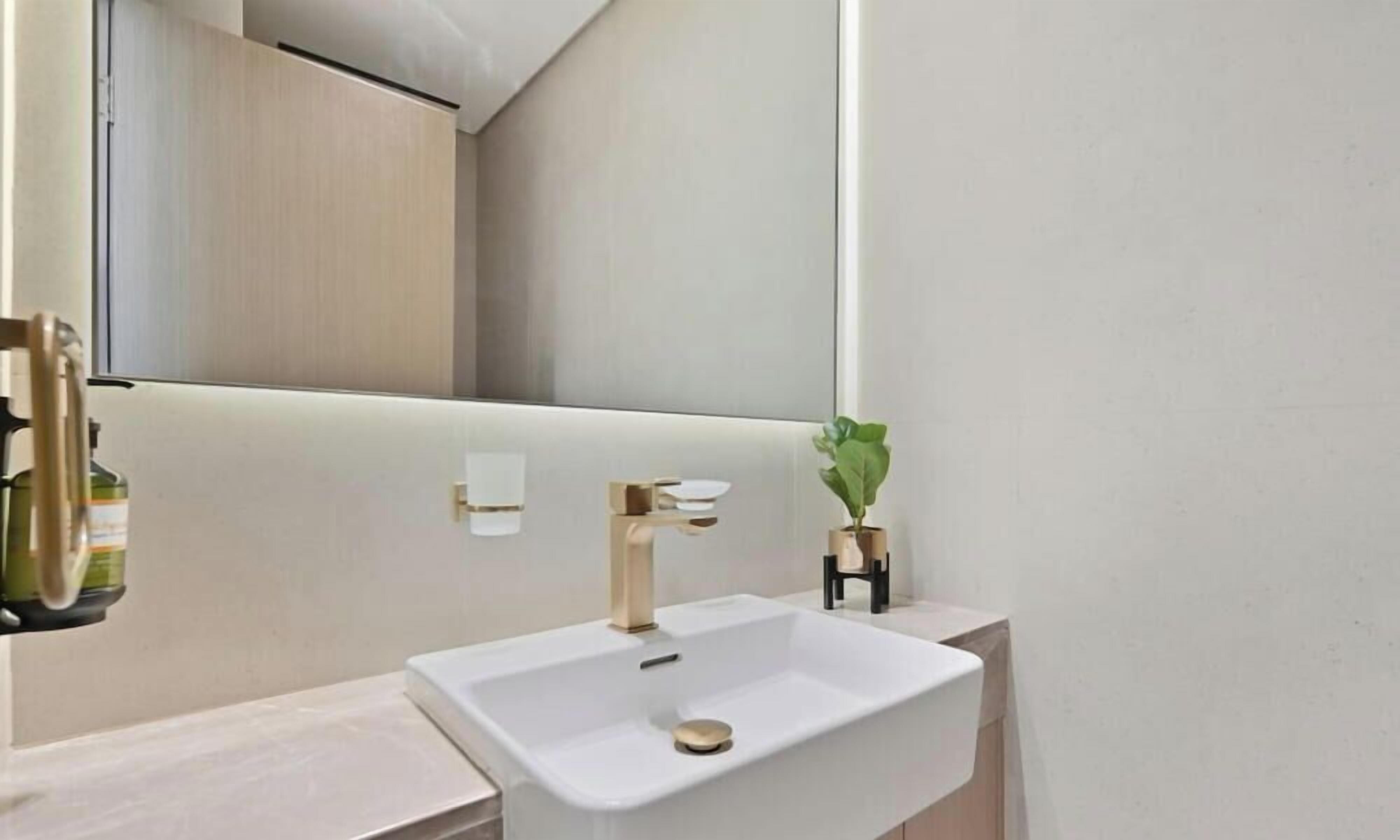 Ein modernes Badezimmer mit einem weißen Waschbecken, einem goldenen Wasserhahn und einem Spiegel darüber.