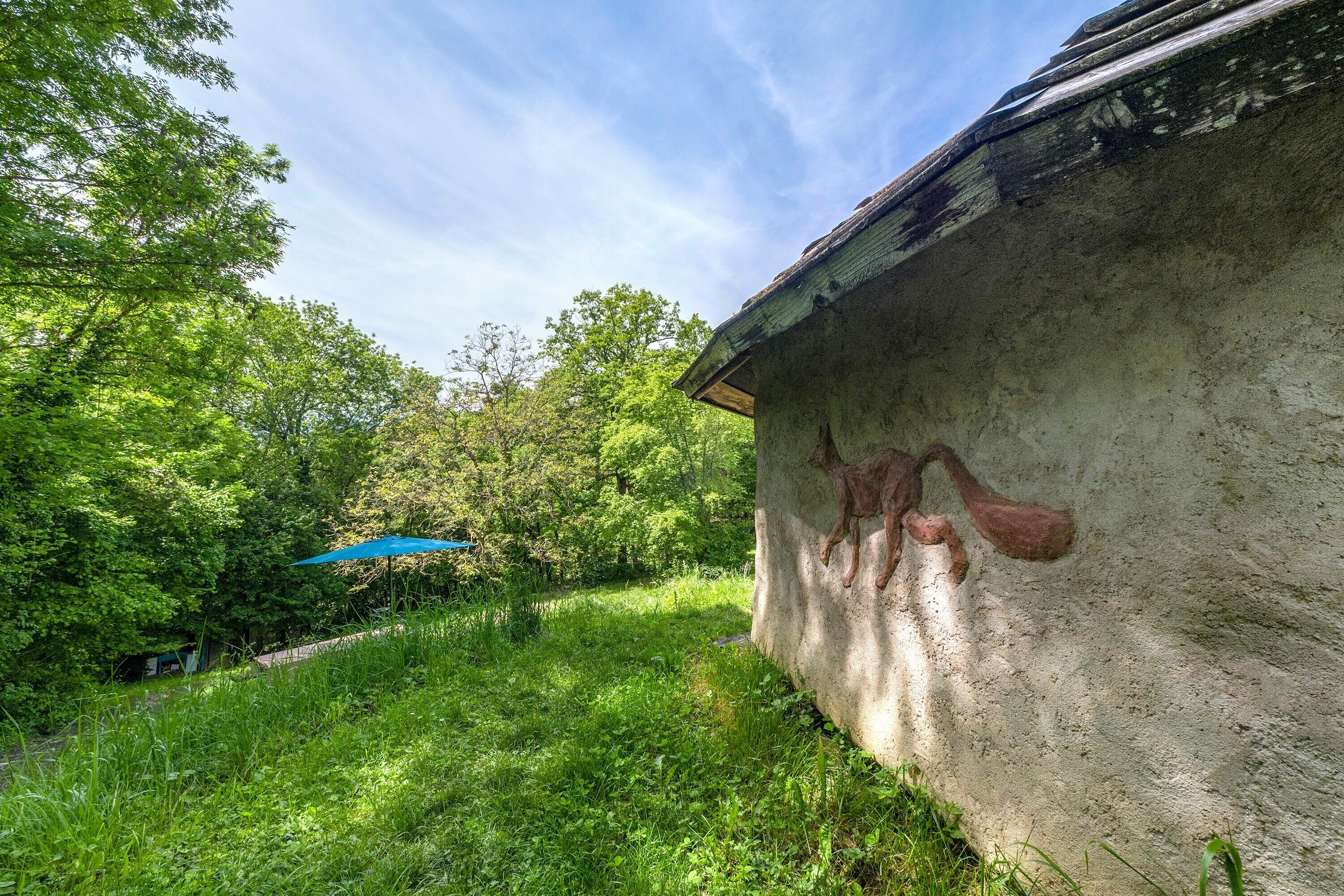 Un mur de béton orné d’une fresque, entouré d’une végétation luxuriante et sous un ciel dégagé.