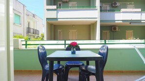 A balcony with a table and chairs, a vase with flowers, and a view of adjacent buildings. - Bilocale Robinia 1 in Baia Verde (Gallipoli)