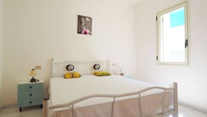 Un dormitorio con cama, mesita de noche, lámpara y ventana.