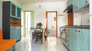 A compact kitchen with teal cabinets, a dining area with a table and chairs, and a bed in the adjacent room. - Robinia 2 Baia Verde - 3 Posti Letto - Posto Auto (Gallipoli)