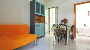 A room with a teal cabinet, orange sofa, dining table with chairs, and a bed. - Robinia 2 Baia Verde - 3 Posti Letto - Posto Auto (Gallipoli)