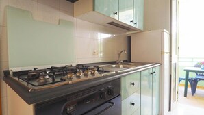 A kitchen with a gas stove, stainless steel sink, and light green cabinets. - Robinia 2 Baia Verde - 3 Posti Letto - Posto Auto (Gallipoli)