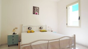 A bedroom with a bed, bedside table, lamp, and a window. - Robinia 2 Baia Verde - 3 Posti Letto - Posto Auto (Gallipoli)